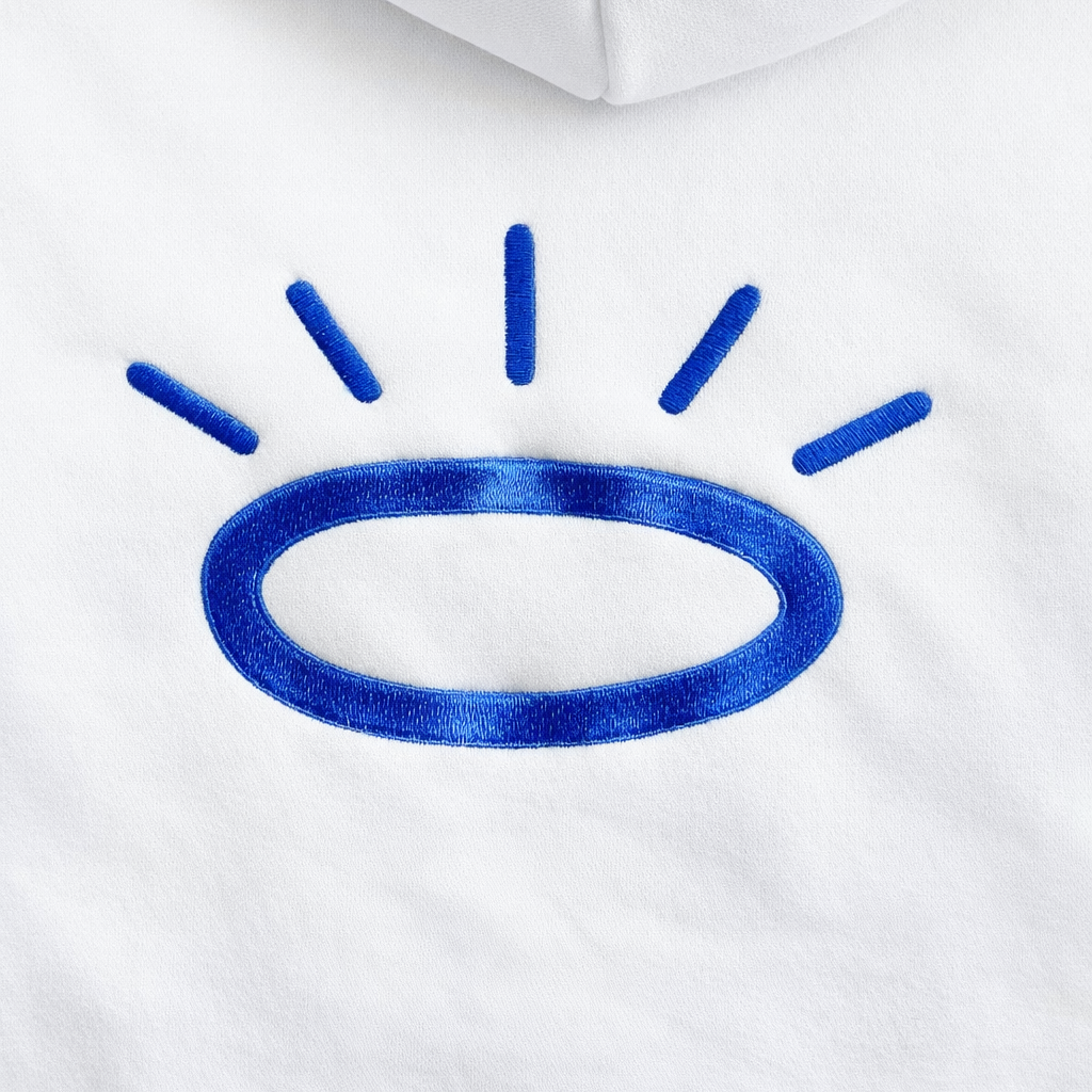 Close-up of halo in Tahoe Blue Tatami embroidery on cream hoodie, showing flat woven stitching with subtle sheen.