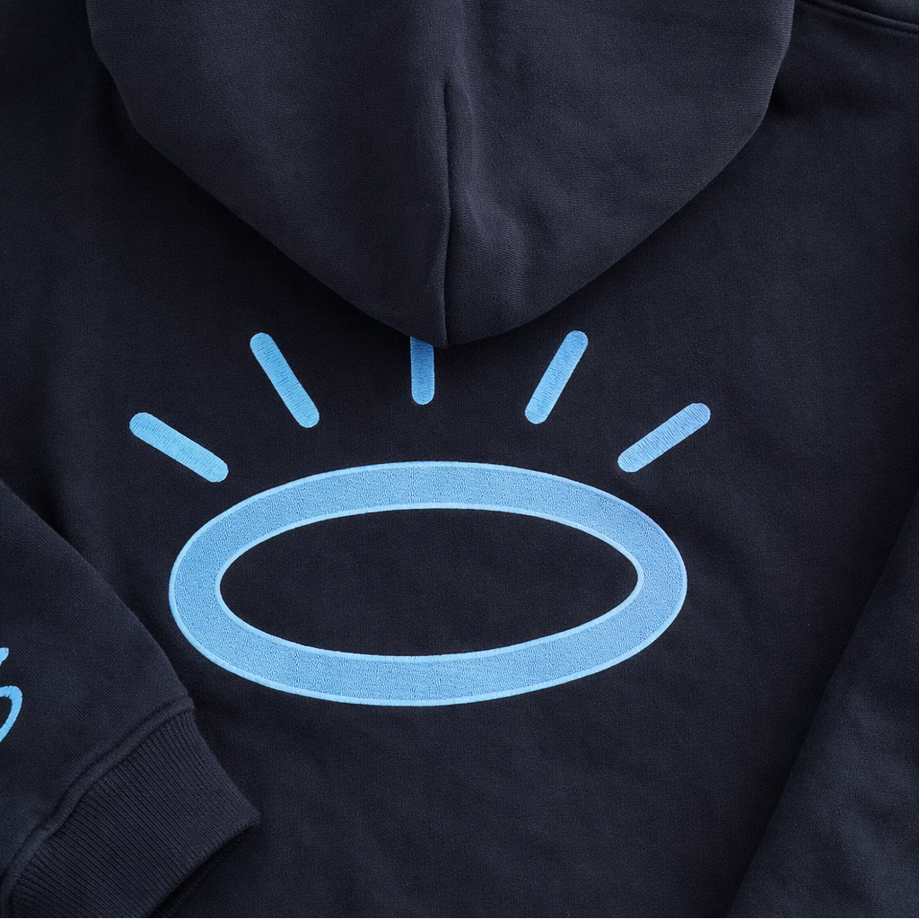 Close-up of Tahoe Blue Tatami embroidered halo on jet black hoodie, showing flat woven stitching with subtle sheen.